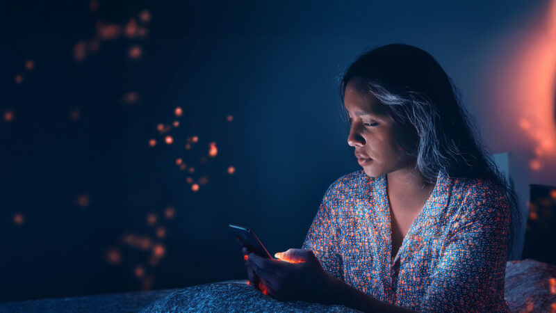 A person using a smartphone at night, representing emotional vulnerability and the human impact of online romance scams linked to so-called “Yahoo Boys”.