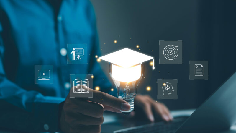 Person holding a glowing lightbulb with graduation cap and digital learning icons on a laptop screen, illustrating AI in education and innovative technology-driven learning.