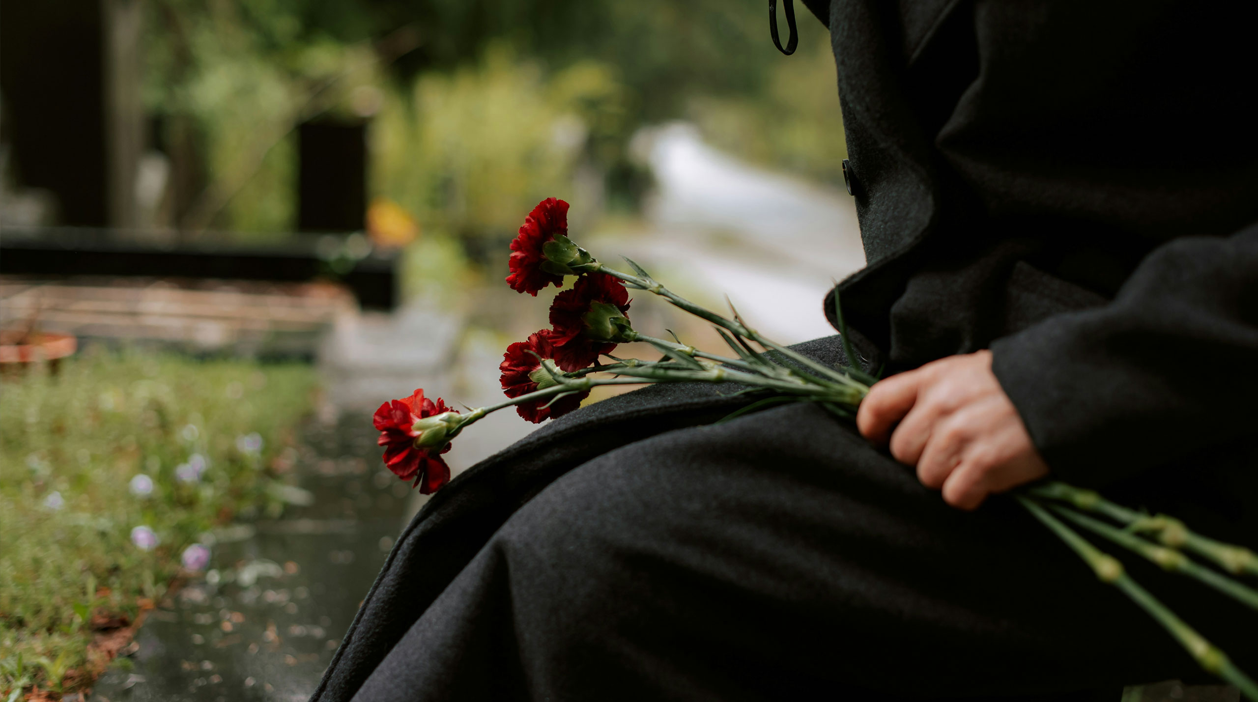 Screenshot of a person in mourning holding red flowers at a gravesite, representing traditional grief in contrast to emerging GriefTech practices that digitally recreate the deceased.