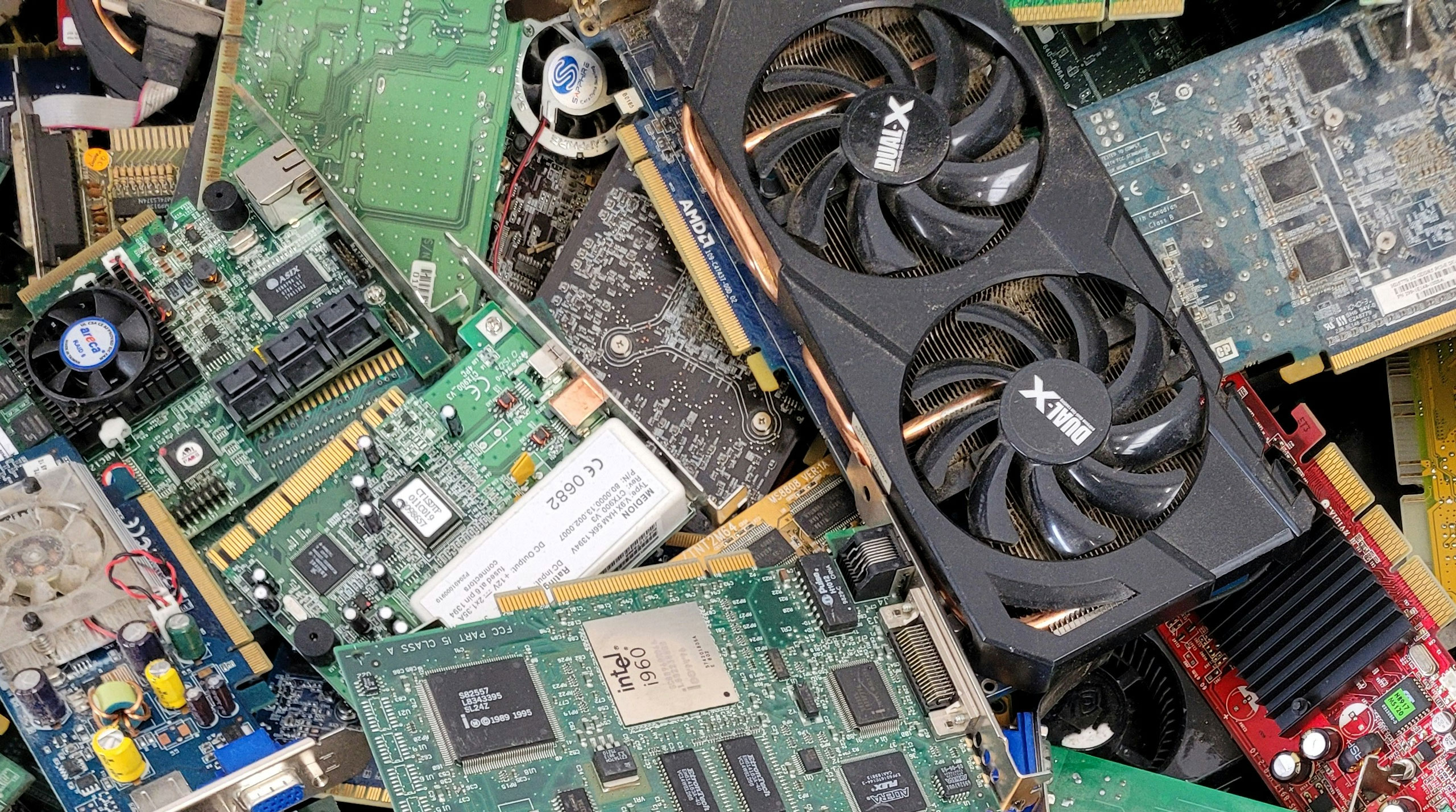 Close-up of E-waste showing a large pile of obsolete computer parts, including graphics cards, motherboards, circuit boards, and electronic components awaiting recycling and responsible disposal.
